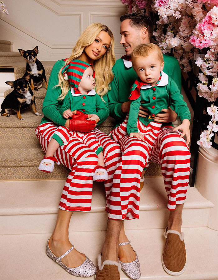 Family in festive attire with two children and dogs, sitting on stairs.