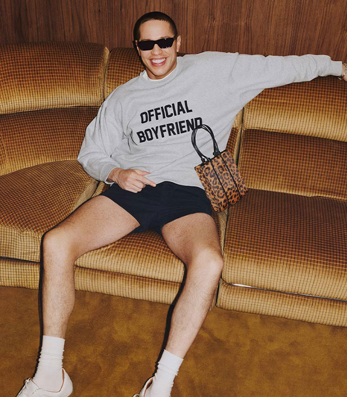 Pete Davidson in a \"Official Boyfriend\" shirt, sunglasses, and shorts, sitting on a couch, showcasing Reformation campaign style.