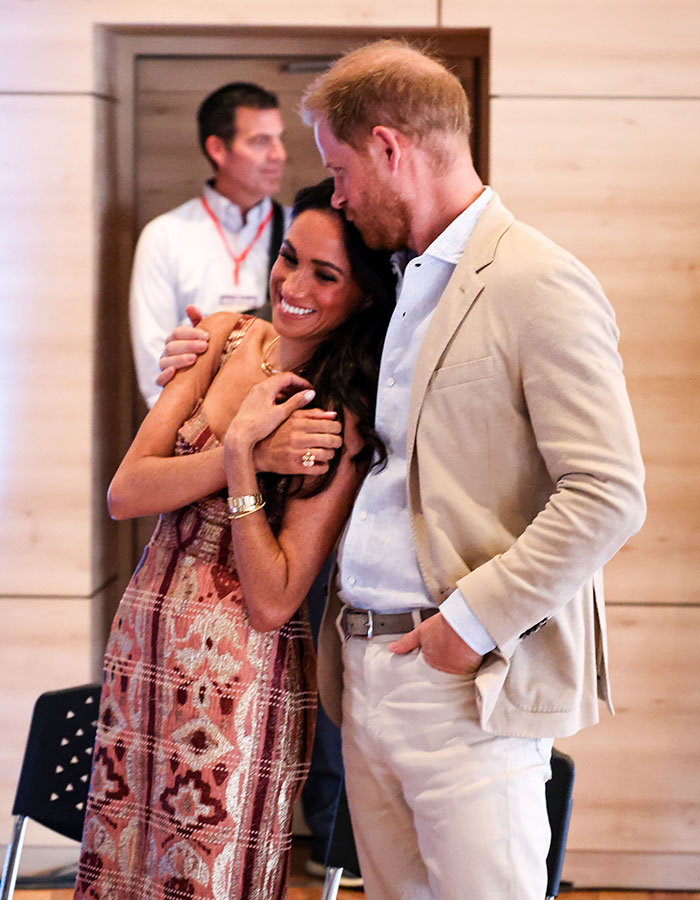 Couple embracing in a bright room, wearing formal attire, with a seated man in the background; Valentine's Day theme.