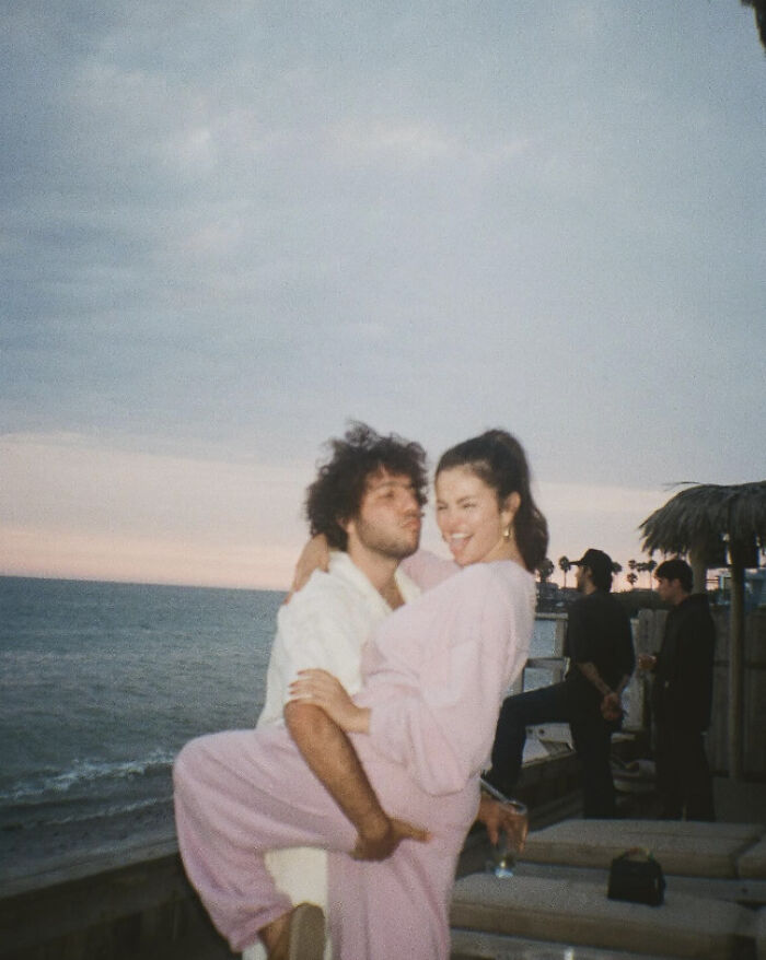 Benny Blanco lifting Selena Gomez, both smiling at a beach setting during Valentine's Day.