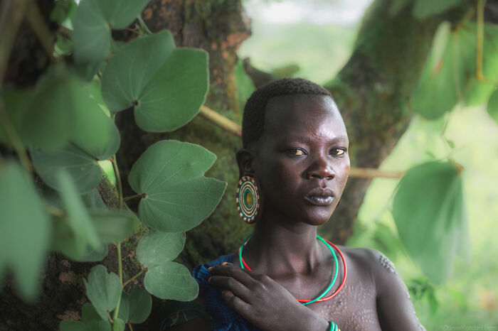 Ethiopian person in traditional attire, surrounded by lush greenery, displaying intricate beaded jewelry.