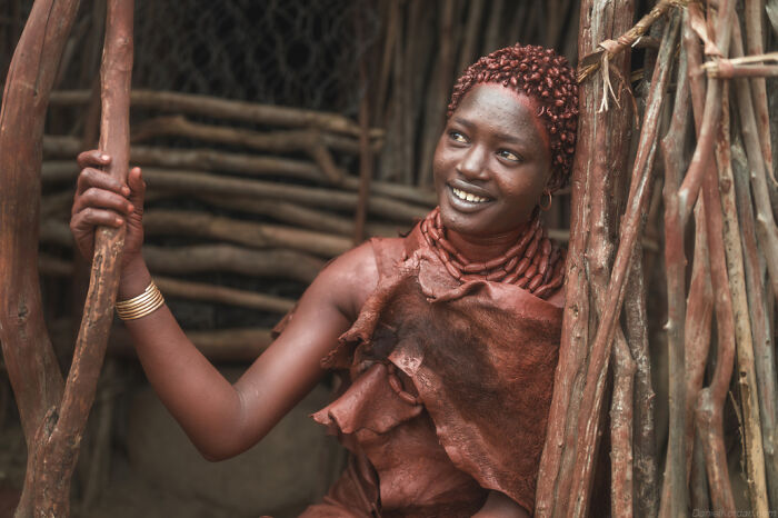 Ethiopian person smiling, wearing traditional attire, against a rustic wooden backdrop.