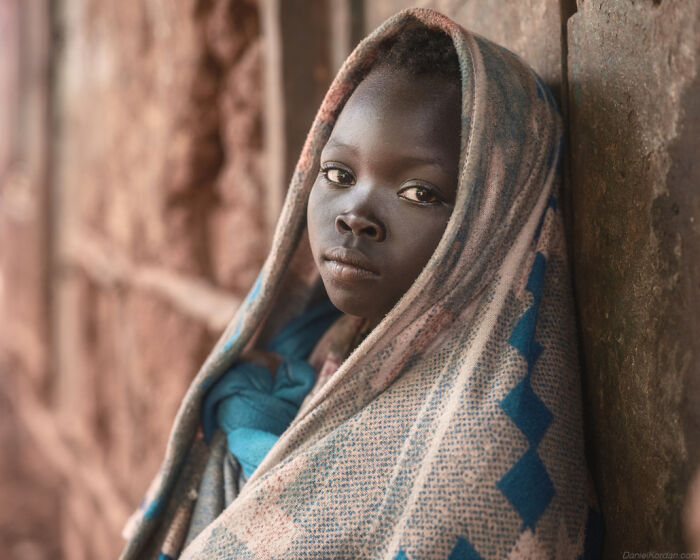 Young Ethiopian wrapped in a patterned shawl, gazing thoughtfully, photographed by Daniel Kordan.