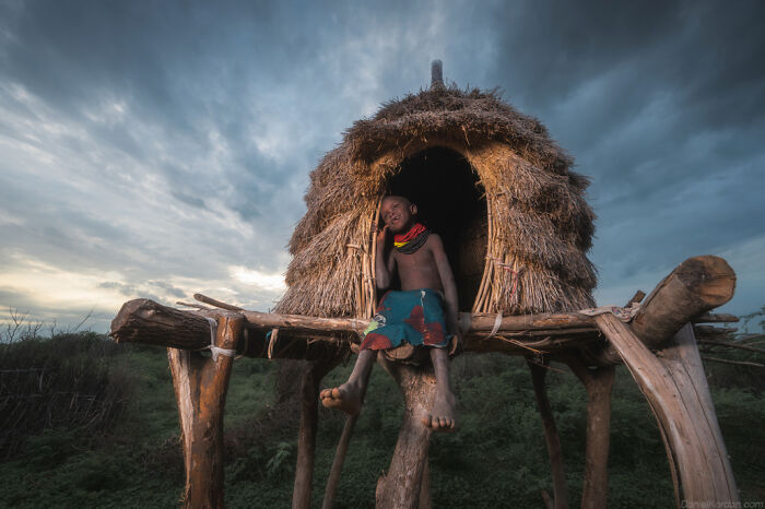 Ethiopian person sitting on a raised, straw hut during sunset, captured by Daniel Kordan.