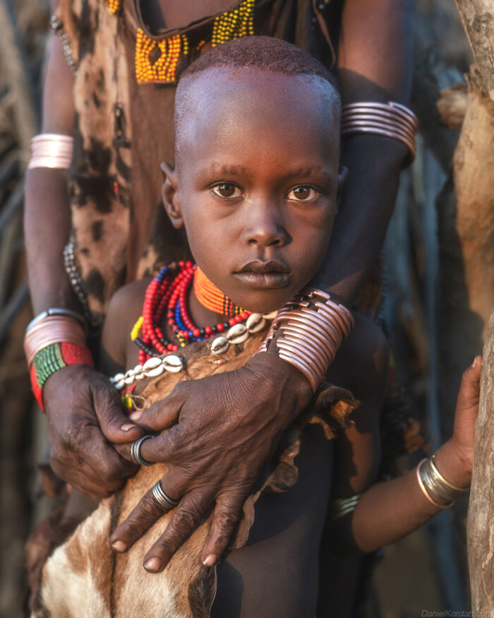 Young Ethiopian child wearing traditional adornments, embraced by an adult, captured in a captivating moment.