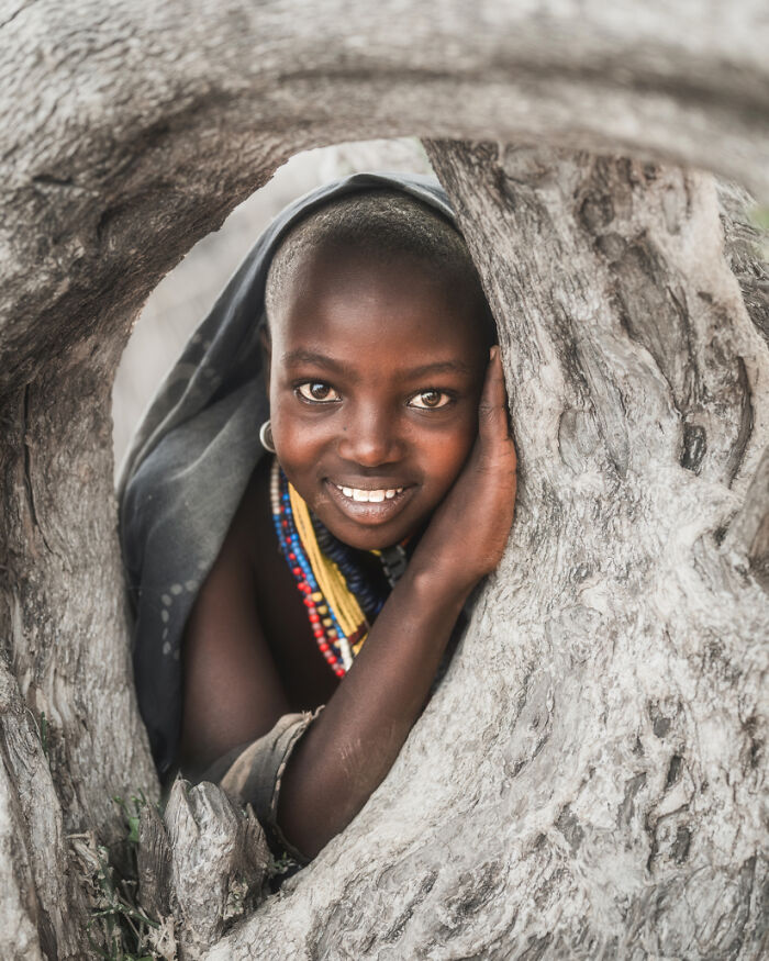 Ethiopian person smiling through a tree, captured in a natural setting by Daniel Kordan.