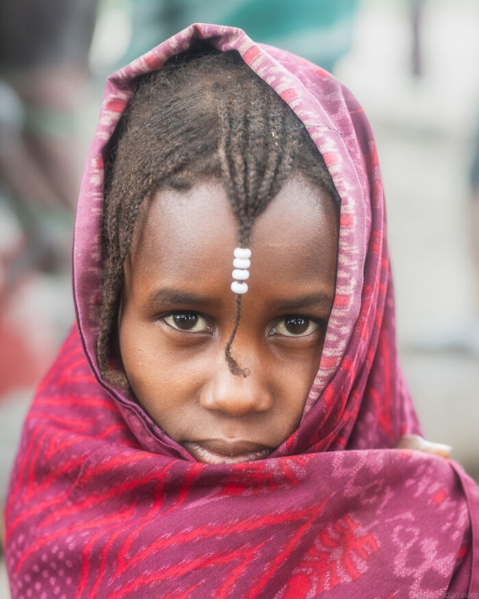 Portrait of an Ethiopian child in a red shawl, featuring intricate braids adorned with beads.