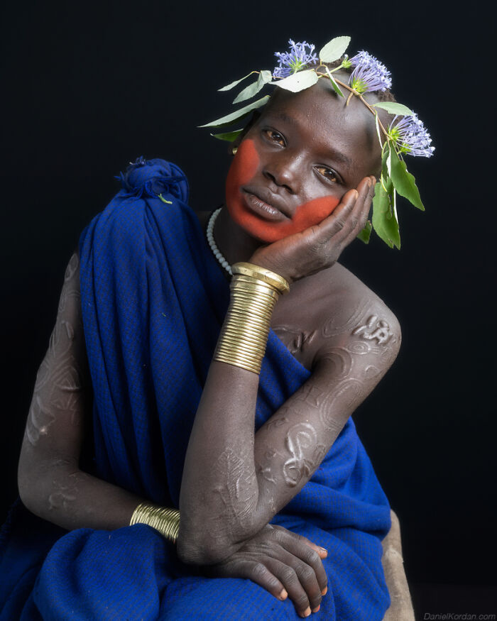 Ethiopian person in traditional attire with floral headpiece, arm bangles, and face paint, captured by Daniel Kordan.