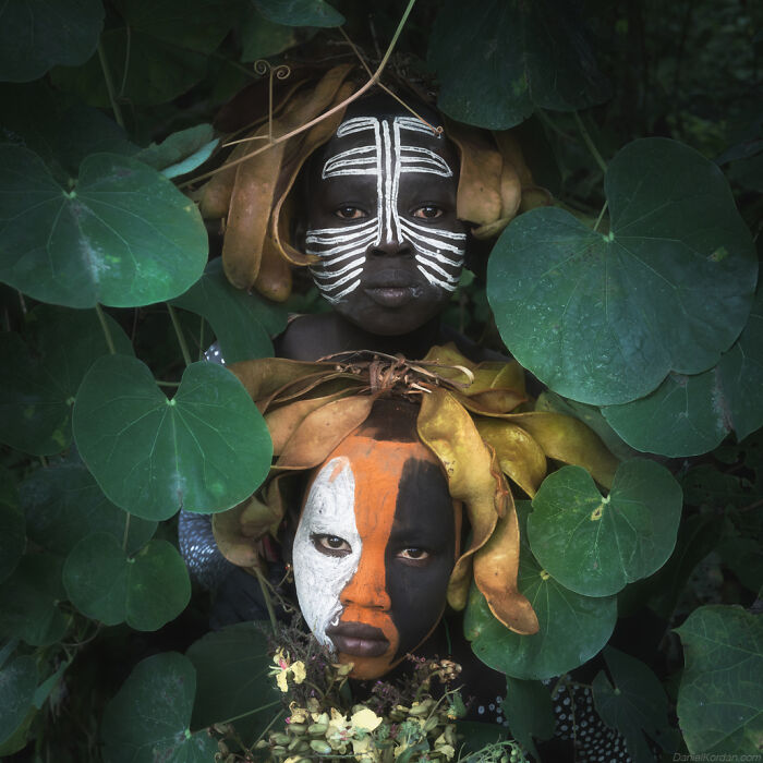 Ethiopian people with traditional face paint, surrounded by lush greenery in Daniel Kordan's captivating photograph.