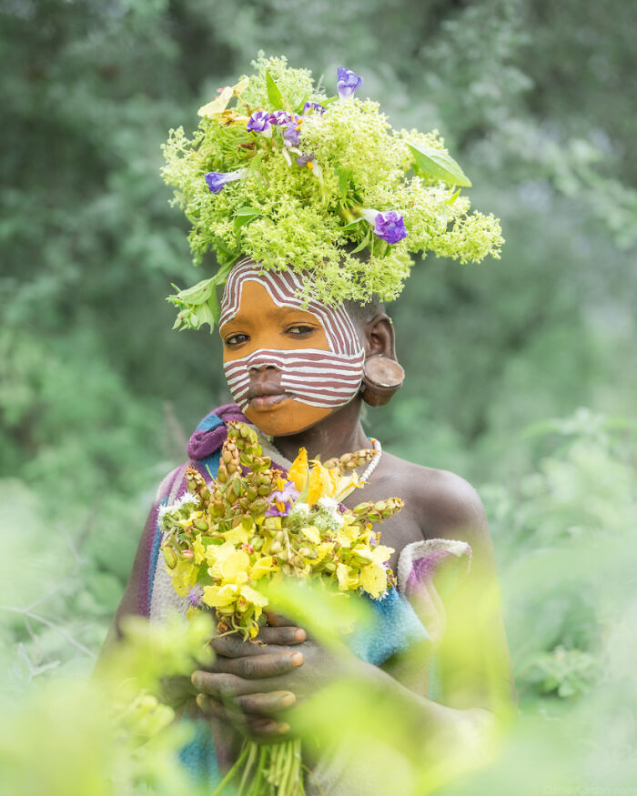 Ethiopian person adorned with face paint and flowers in a natural setting.