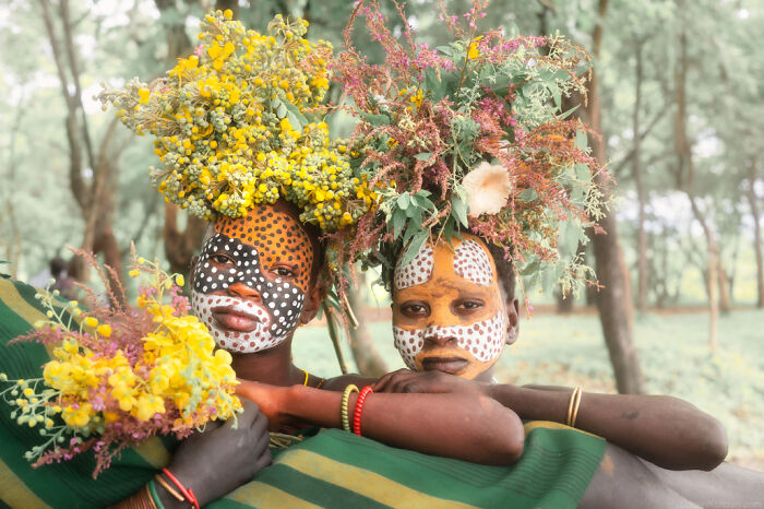 Ethiopian people with painted faces and floral headpieces, showcasing vibrant cultural expressions in nature.