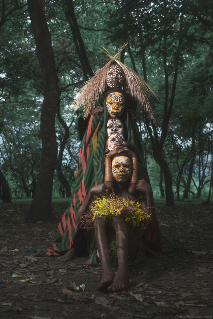 Ethiopian person with painted face and floral decorations in a forest, captured by Daniel Kordan.