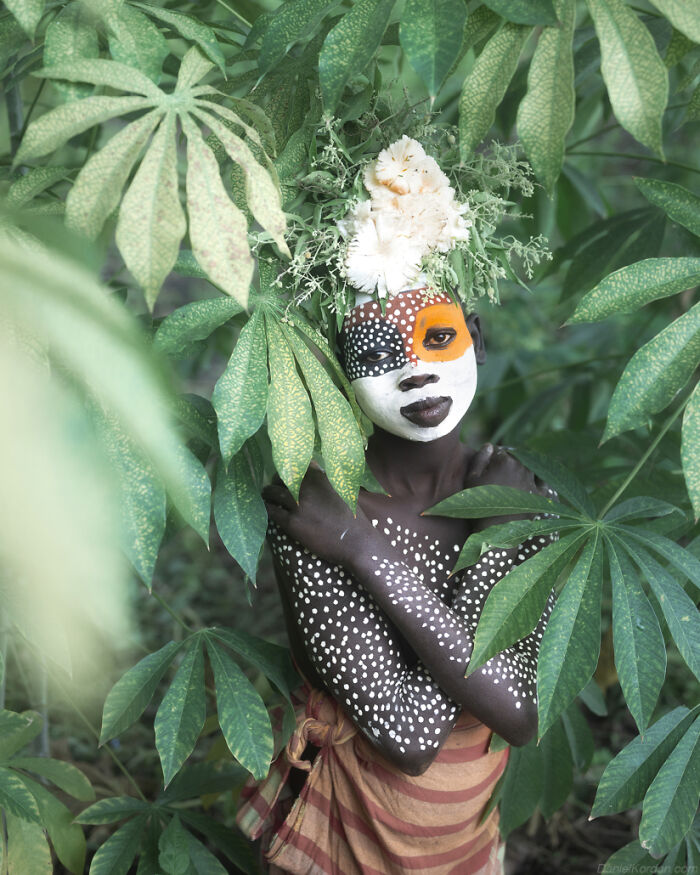 Ethiopian person with face paint and floral headdress in lush greenery, captured by Daniel Kordan.