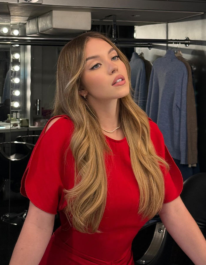 Young woman in a red dress posing in front of a mirror with lights.