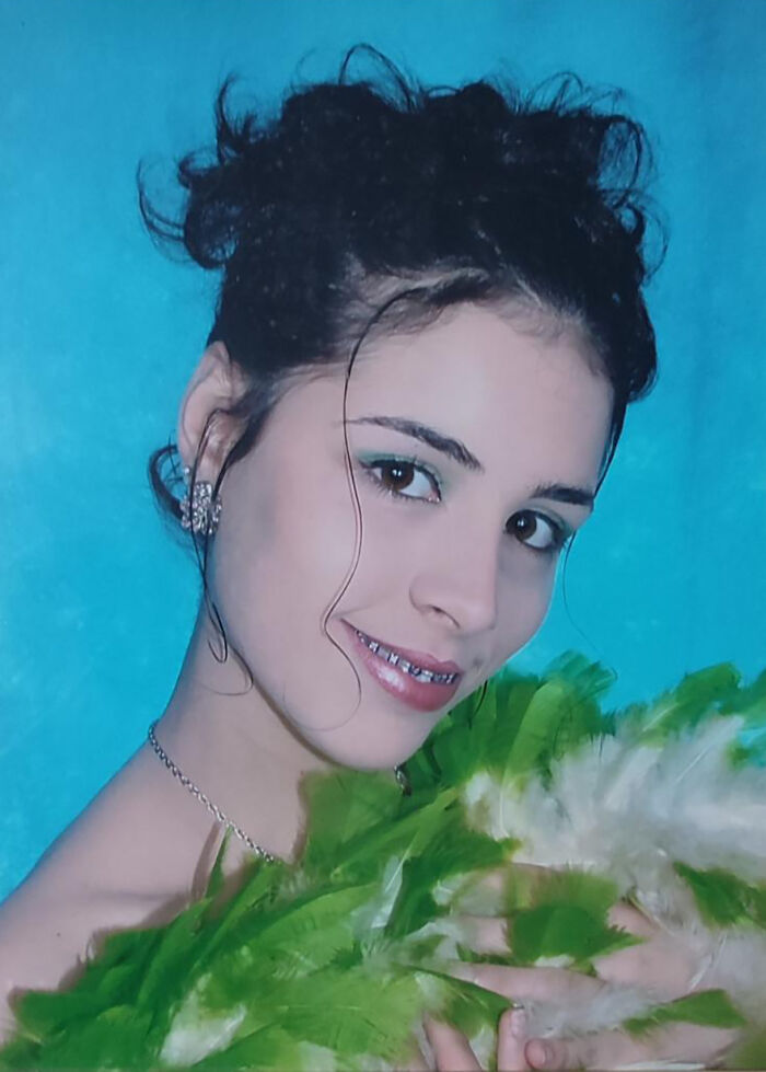 \"Smiling woman with curly hair and jeweled earrings, holding green feathers, in front of a blue background.\