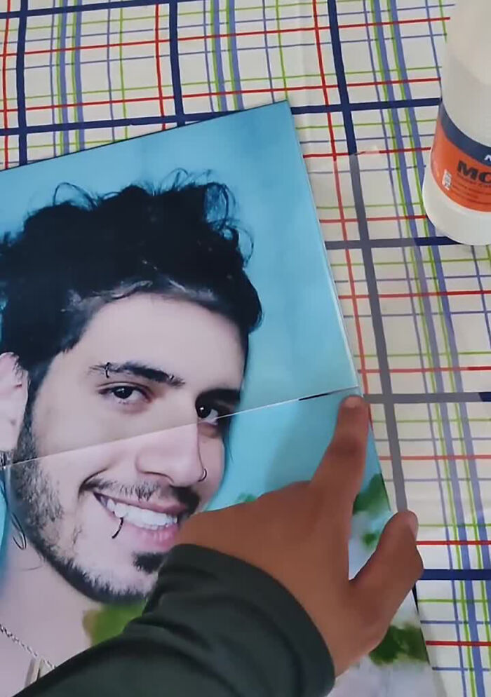 A person pointing at a cutout photo on a colorful grid tablecloth, part of a funny prank on family.