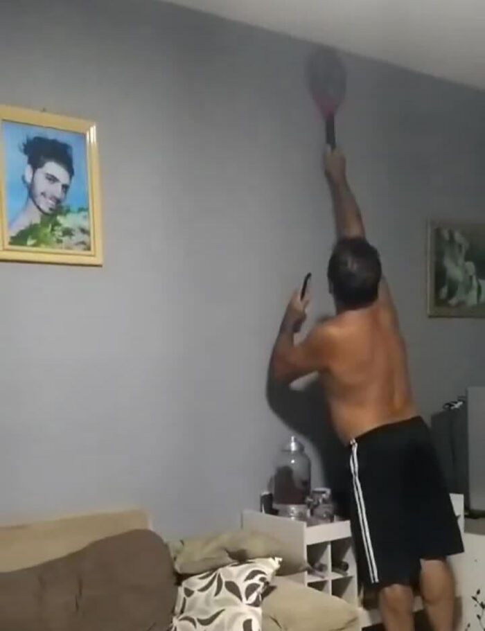 A man pranking his family, reaching with a tennis racket in a living room, captured in a humorous moment.