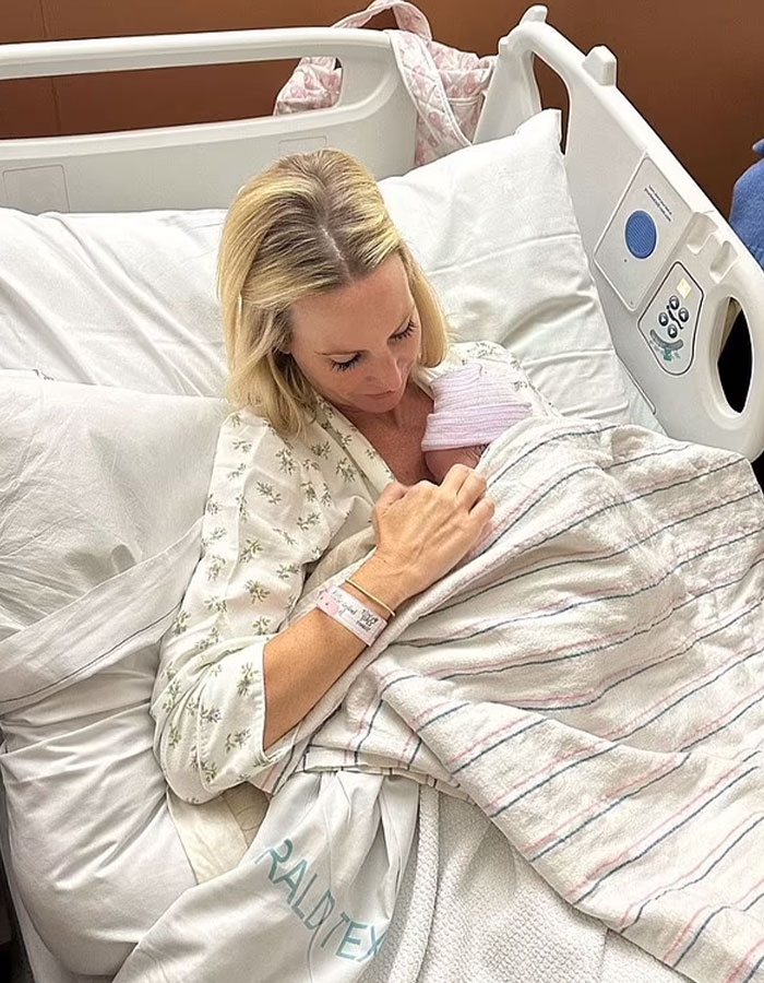 Celebrity in hospital bed holding surrogate baby wrapped in a blanket.