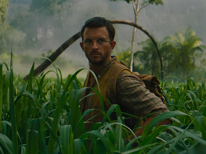 Jonathan Bailey with glasses and a backpack in a jungle setting.