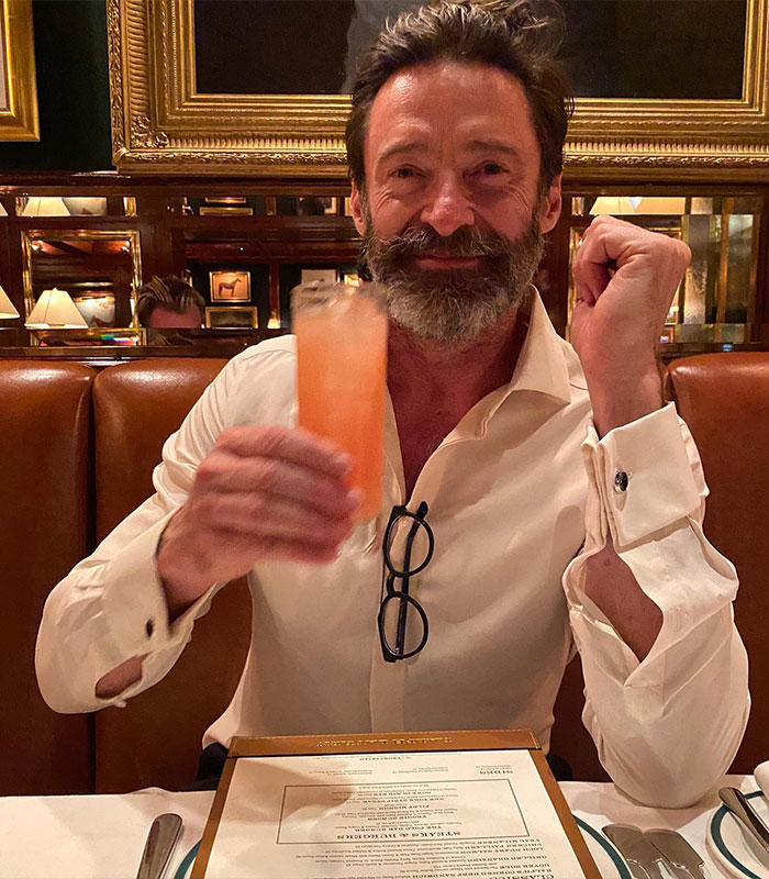 Man in a restaurant holding a pink drink, wearing a white shirt and glasses, looking pleased.