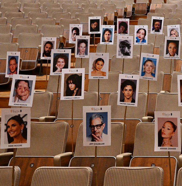 Empty auditorium with seats showing celebrity name cards, including Adam Pearson.