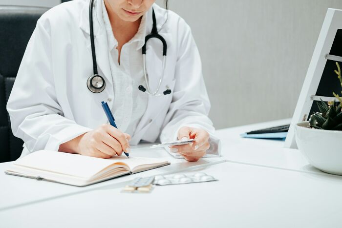 Doctor in a white coat writes notes at a desk, holding a prescription, related to female body facts.