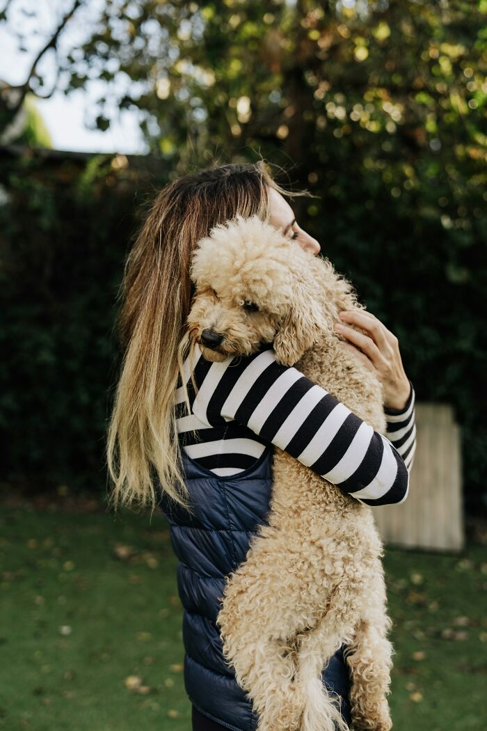 Woman in striped sweater hugging a curly-haired dog in a garden, offering a fresh perspective on world affection.