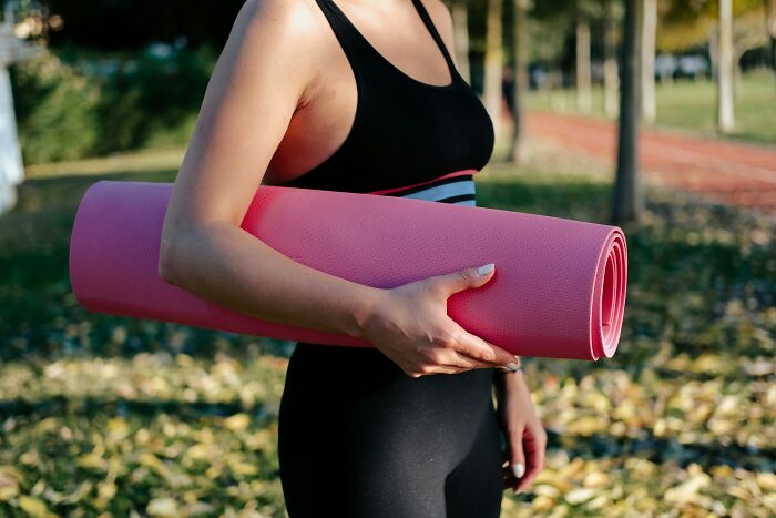 Person holding a pink yoga mat outdoors, highlighting travel must-have gear.