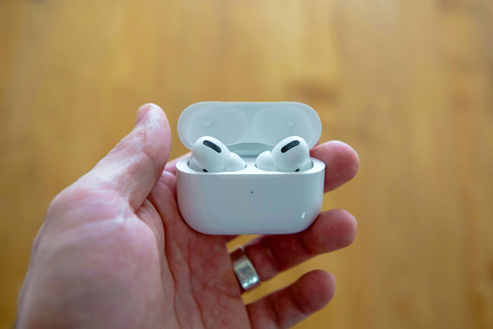 Hand holding noise cancelling AirPods in a white case, showcasing sleek design against a blurred background.