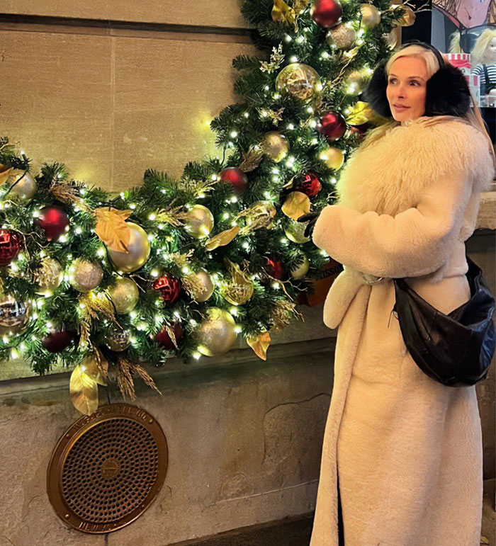 Woman in a fur coat and earmuffs beside a decorated Christmas wreath, related to Bianca Censori controversy.