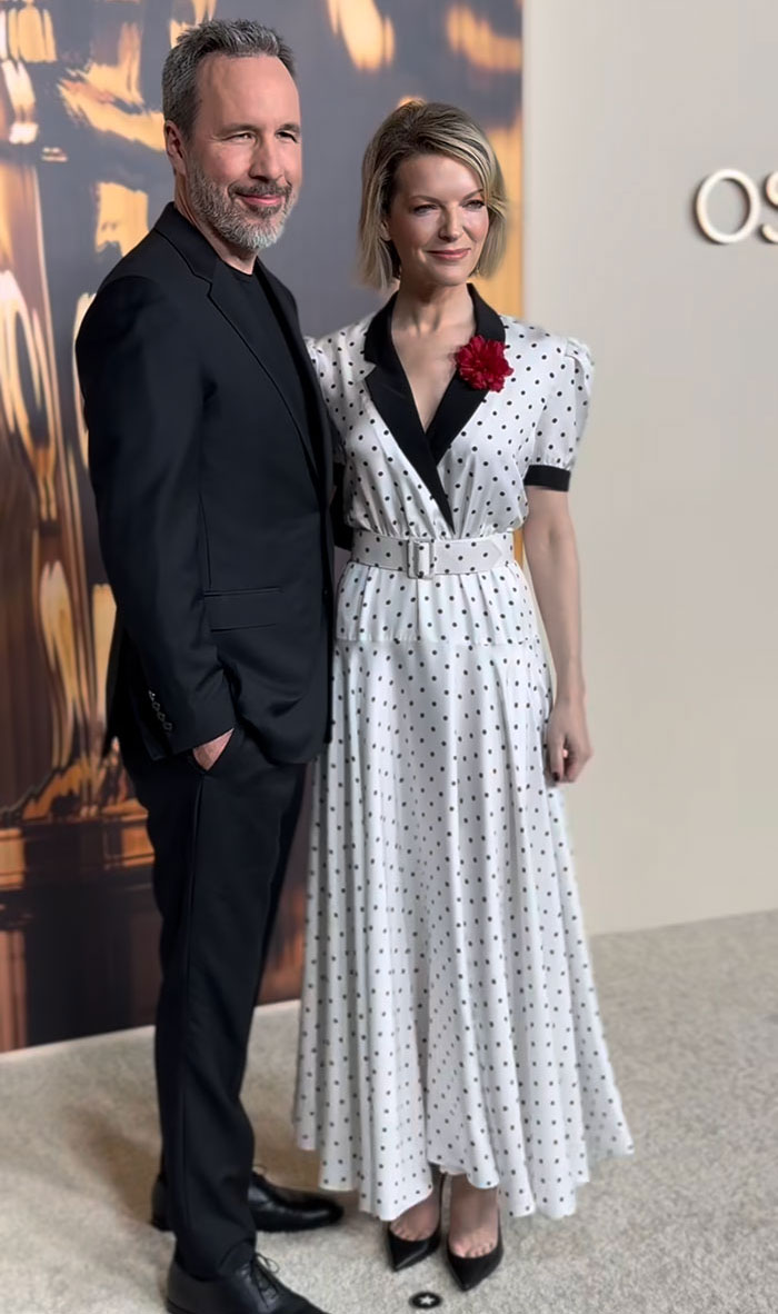 Man in suit and woman in dotted dress at 2025 Oscar nominees dinner, showcasing fashion triumphs.