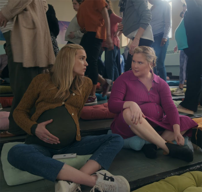 Two women sitting on floor cushions, discussing in a casual setting, related to comedy and viewer reactions.