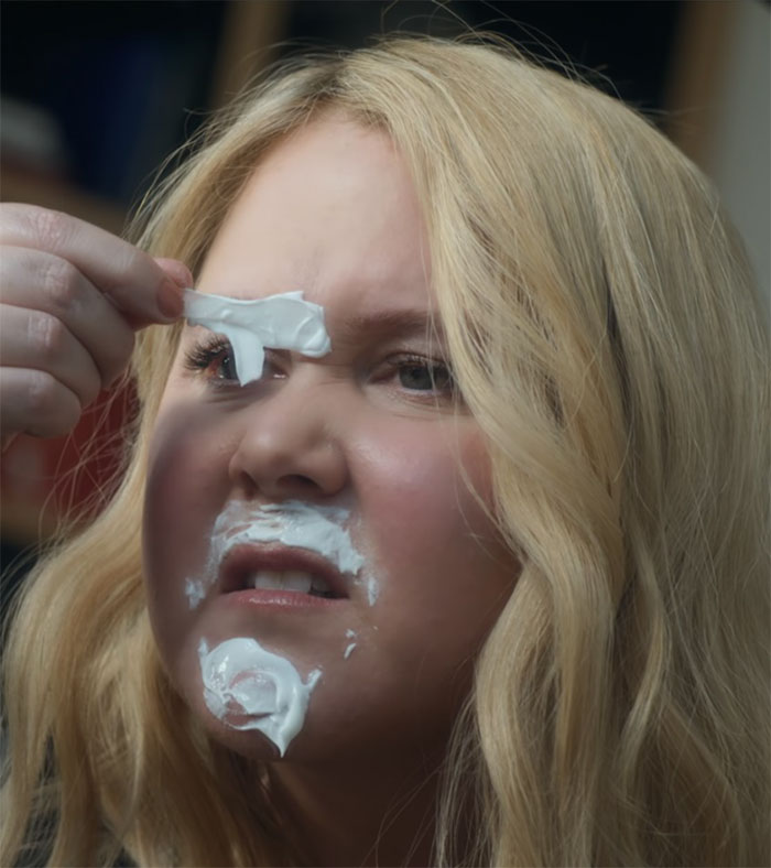 A woman with blonde hair making a funny face, removing cream from her face, in a comedic scene.