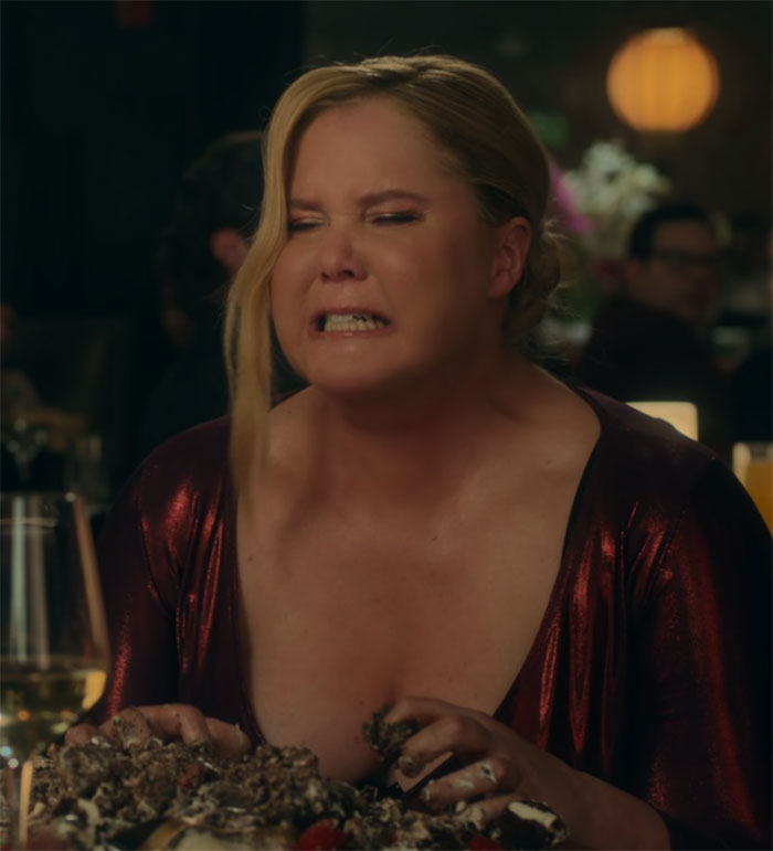 Amy Schumer at a dining table, looking distressed, from her new comedy skit.