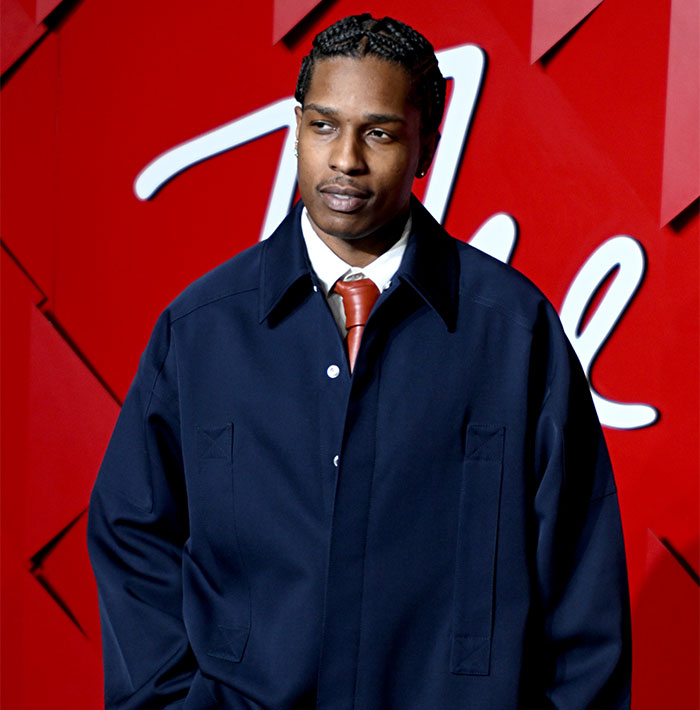 Young man in a navy coat and red tie at an event, amid Met Gala dress code controversy.