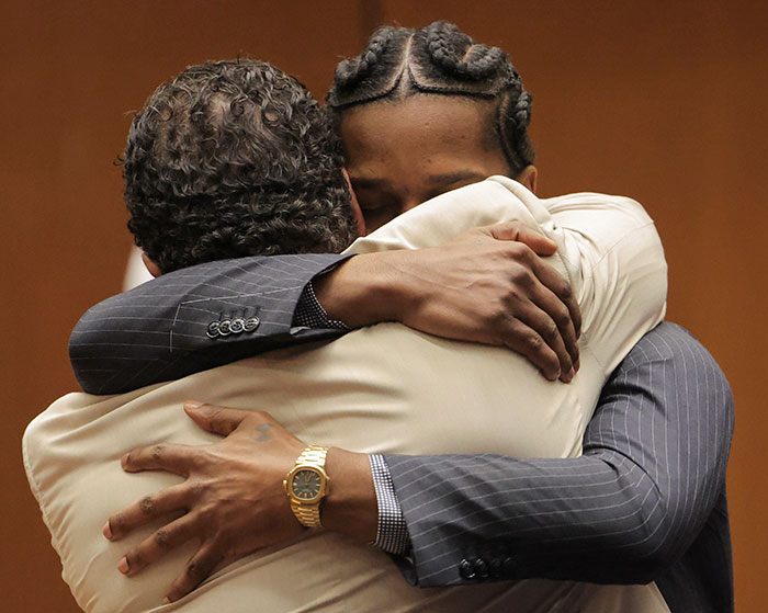 Two men in suits embrace emotionally in a courtroom setting.