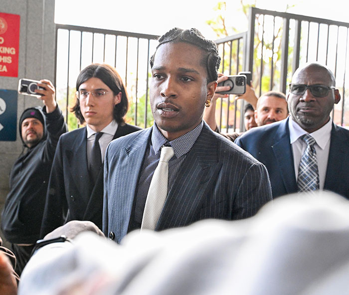 Person in a striped suit walking past cameras, related to a felony assault trial.