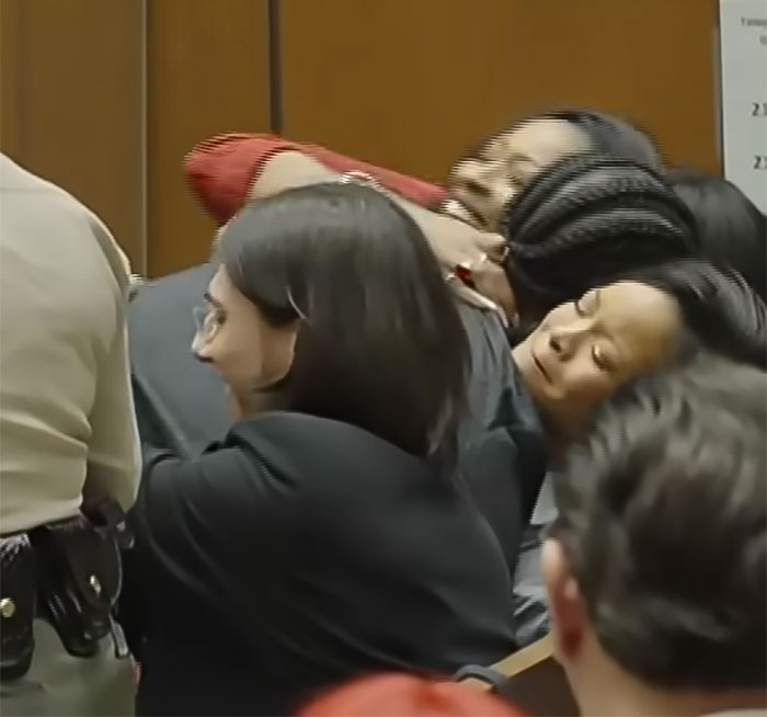 People embracing emotionally in a courtroom setting after a trial.