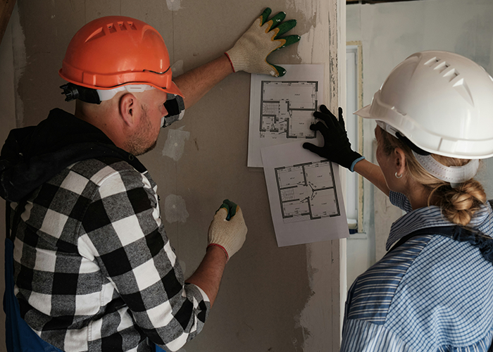 Two workers in hard hats examining floor plans for a cabin restoration.