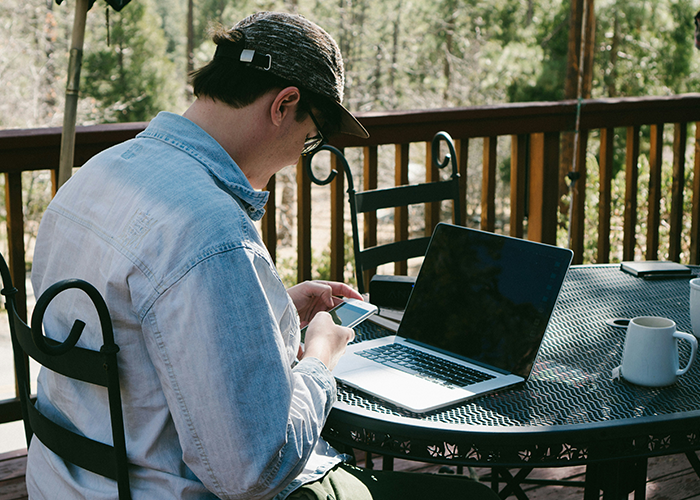 Person using a phone and laptop on a cabin deck with trees in the background, highlighting family cabin use.