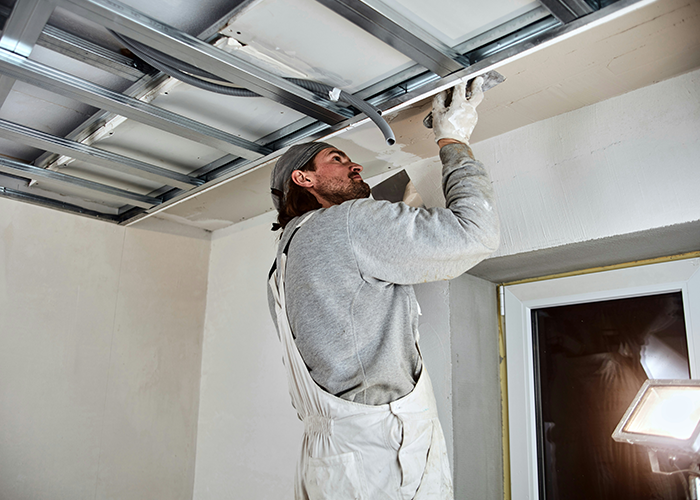 Person restoring a cabin ceiling, wearing work clothes and using a trowel, with a focus on renovation and repair efforts.