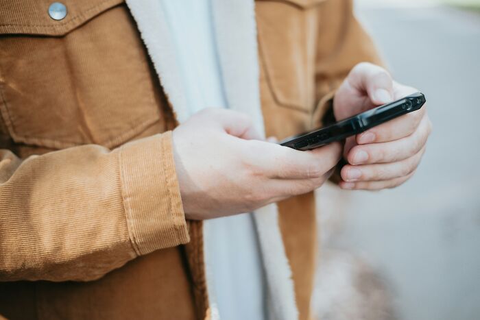 Person in a tan jacket holding a smartphone, connected to Gen Zers' opinions on Boomer complaints.