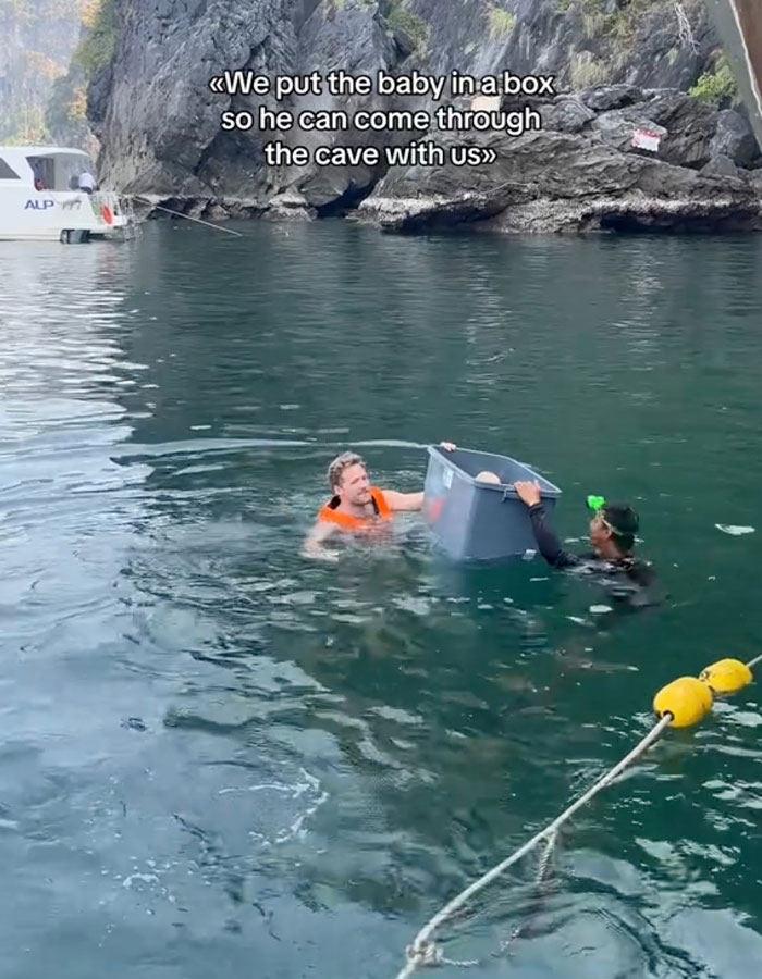 Parents transporting baby in plastic box through cave waters in Thailand.