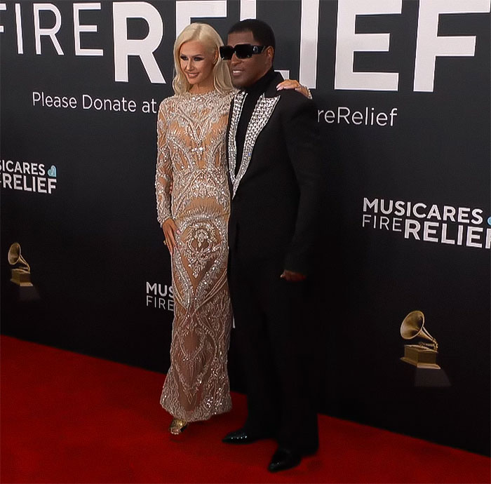 Couple on the red carpet at MusiCares event, standing against a Fire Relief backdrop.