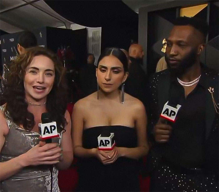 Three reporters with microphones during the Grammys event, discussing Chappell Roan and R&B legend snubbing controversy.