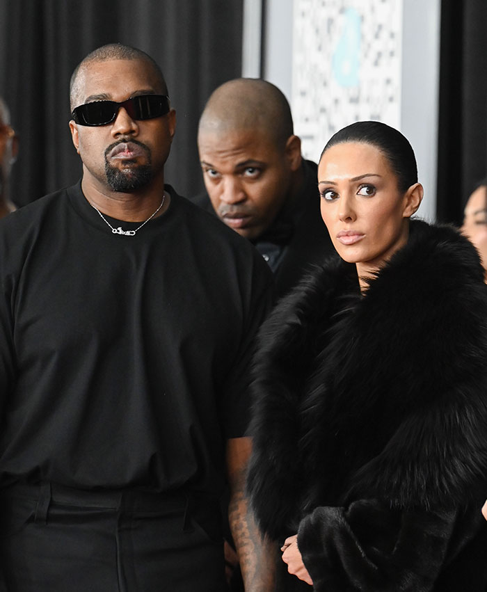 Bianca Censori in a fur coat at the Grammys red carpet with two men beside her.