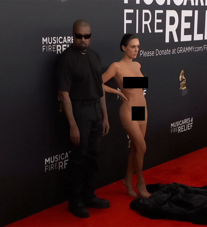 Man and woman on Grammys red carpet; woman in bold outfit, attracting attention.