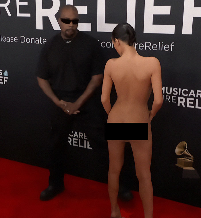 Bianca Censori in controversial dress at Grammys event, standing on red carpet next to a man in black.