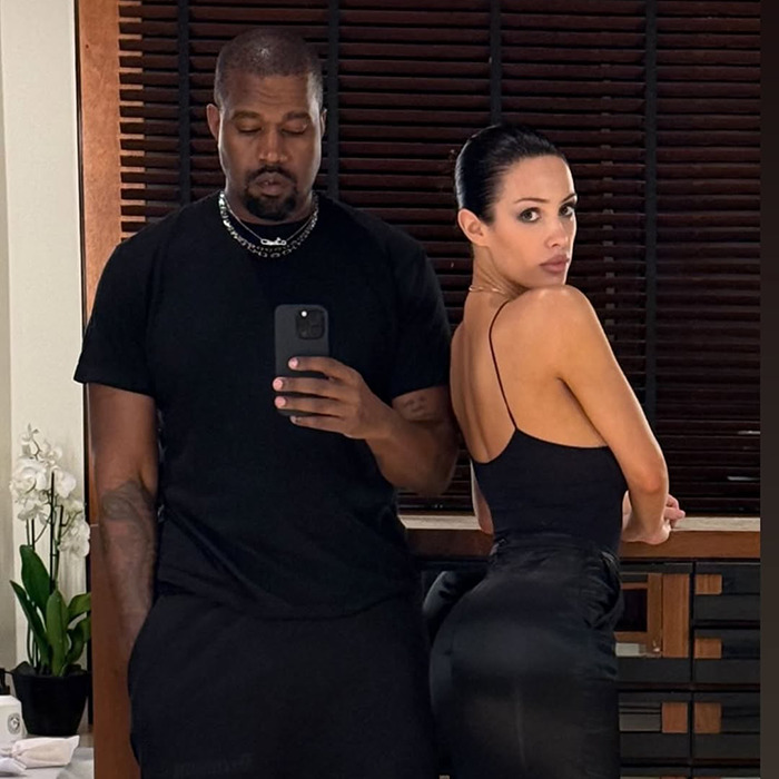 Kanye West and Bianca Censori in all black outfits posing for a mirror selfie indoors.