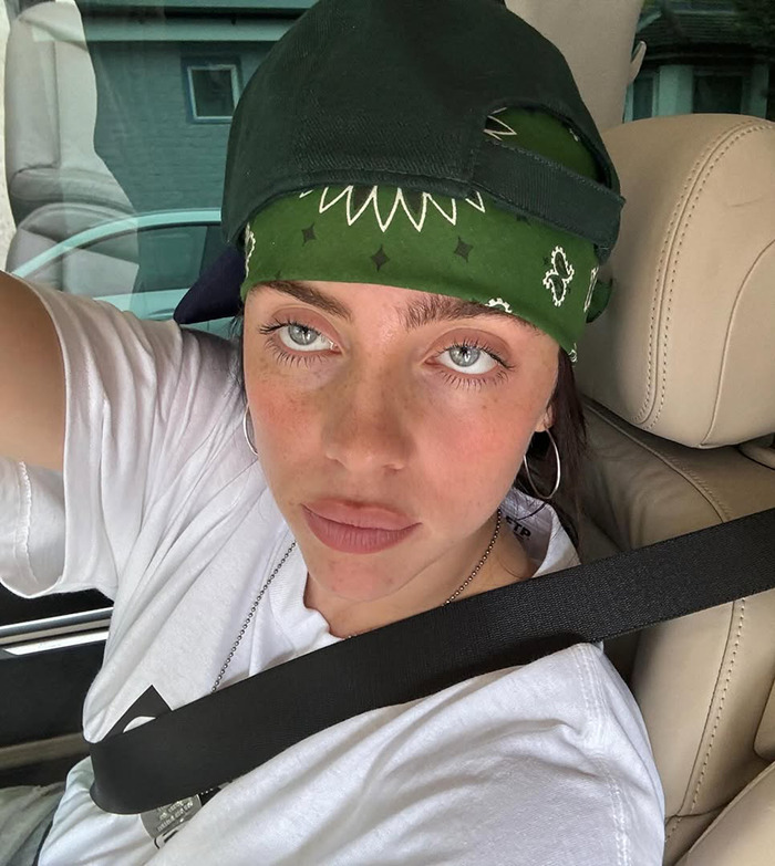 Young woman wearing a green bandana and cap, seated in a vehicle, possibly related to Billie Eilish merch discussion.